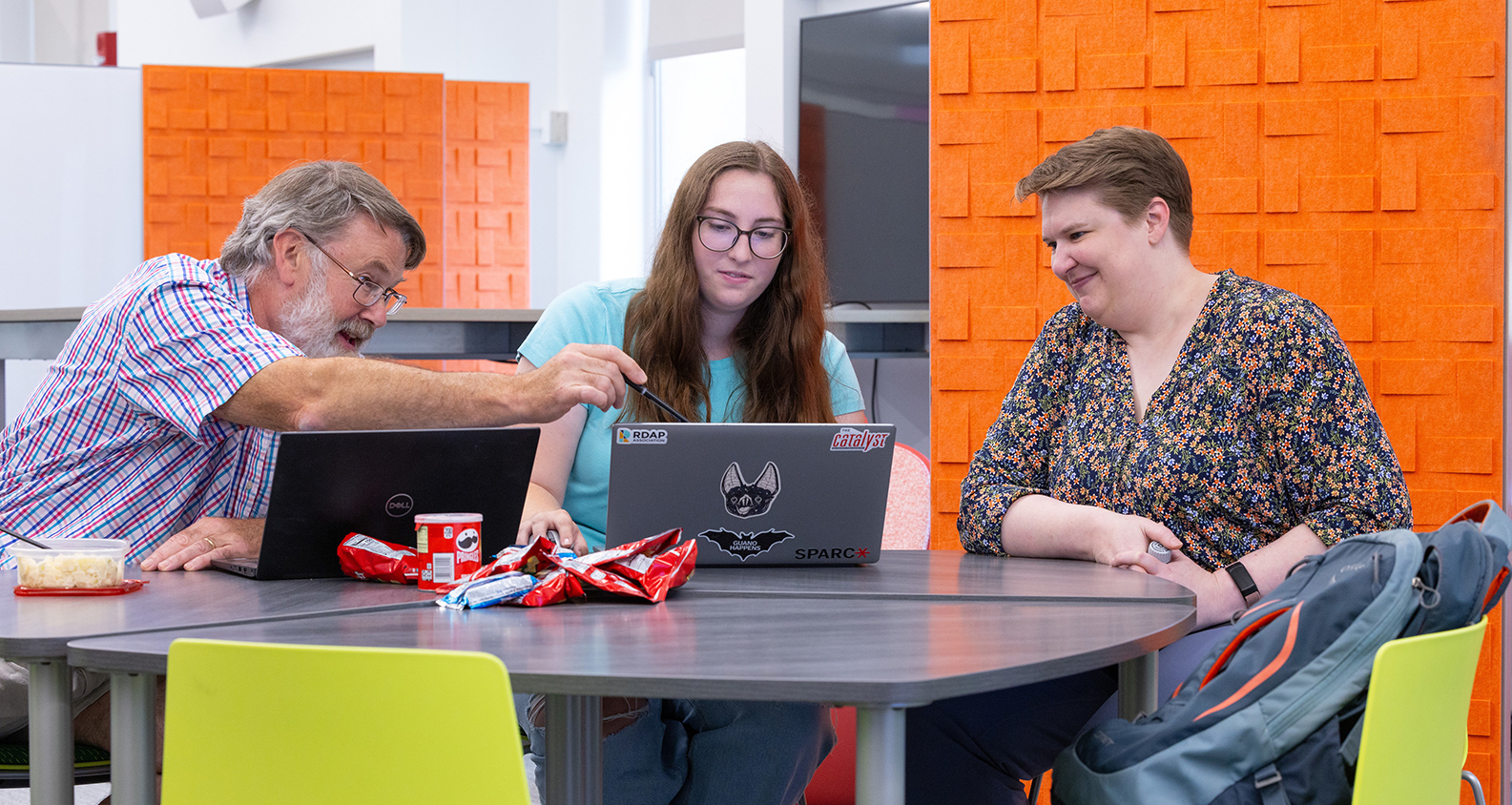 A professor and library help an undergraduate with their research while looking at laptops in the Catalyst 